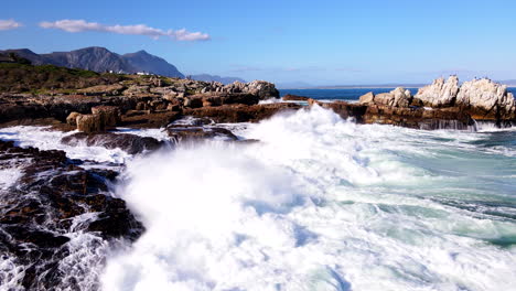 una toma de retroceso de un dron de las olas del océano chocando contra la costa rocosa de hermanus.