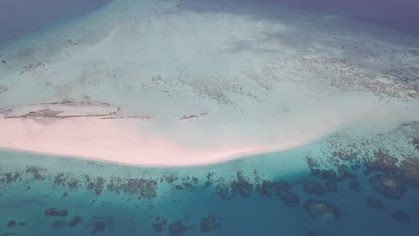 rotating high sea aerial of small sand islet dotted with coral reefs