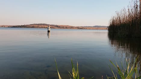 A-girl-fishing-for-bass-while-wading-inside-a-lake-on-a-calm-sunny-day