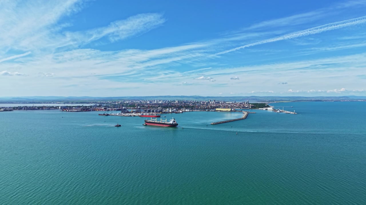 Una nave arriva in un tranquillo porto marittimo. Un drone riprende la scena serena di una nave che si avvicina a un porto calmo. Una nave da carico si avvicina a una baia soleggiata mentre il drone filma la tranquilla vita portuale.