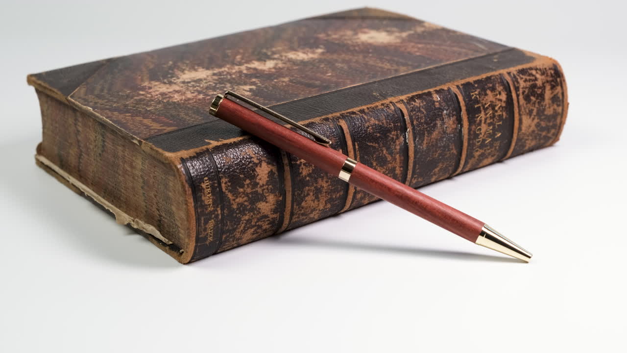 Primo piano di una penna poggiata su un vecchio libro posizionato su un tavolo bianco, creando un concetto di scrittura semplice e minimale, con un'ombra in movimento dalla luce dall'alto