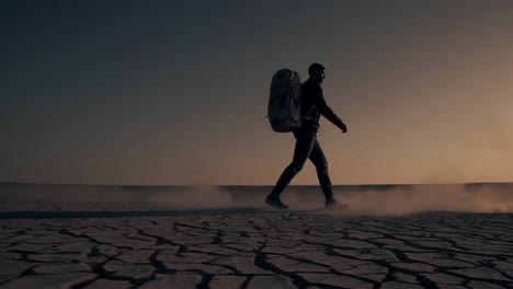 man hiking through a dry desert at sunset