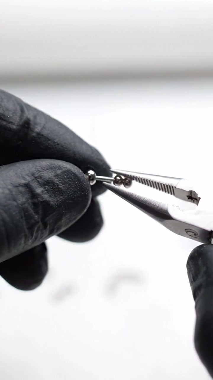 Close-Up of a Hand Using Pliers to Manipulate a Small Metal Object with an Intricate Design, Set Against a Soft White Background for High Contrast