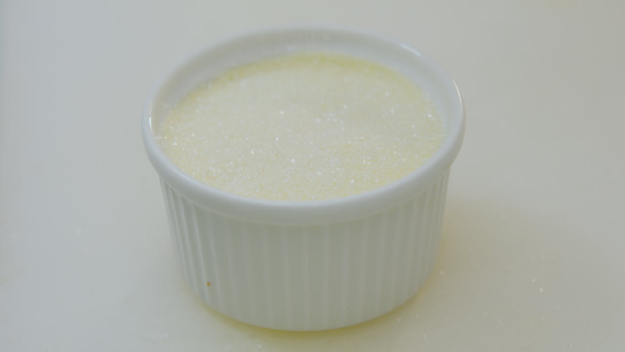 Primo piano di uno chef che spolvera zucchero su una crème brûlée prima di caramellarla
