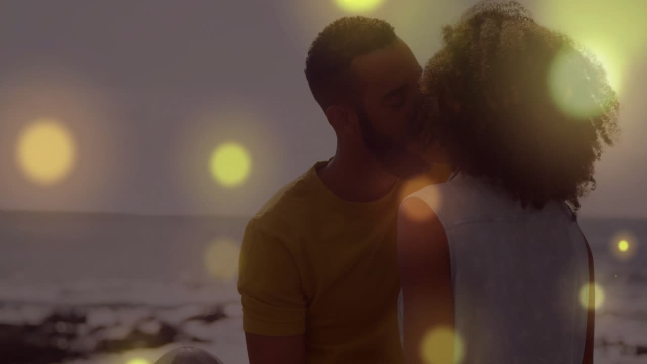 lifestyle showing sunset on rocky beach intensifying golden bokeh couple leaning in sharing kiss
