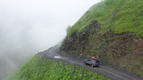 cinematic drone shot of vehicle driving on the edge of a cliff on the road to tusheti going through puddles, one of the worlds most dangerous roads