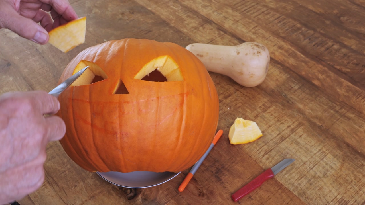 Man carving triangle eyes on pumpkin to create Halloween jack-o’-lantern
