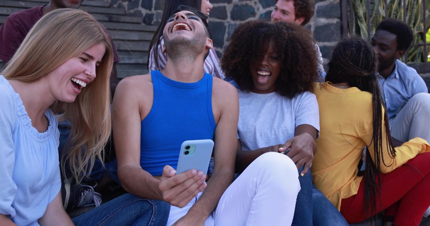 Diverse Freundesgruppe lacht und schaut auf ein Smartphone.