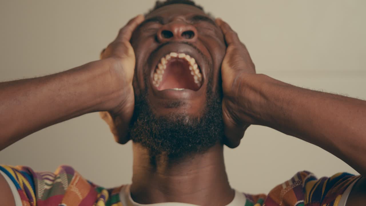 Giovane Uomo Afroamericano Barbuto Depresso e Frustrato che si Tiene la Testa tra le Mani e Piange