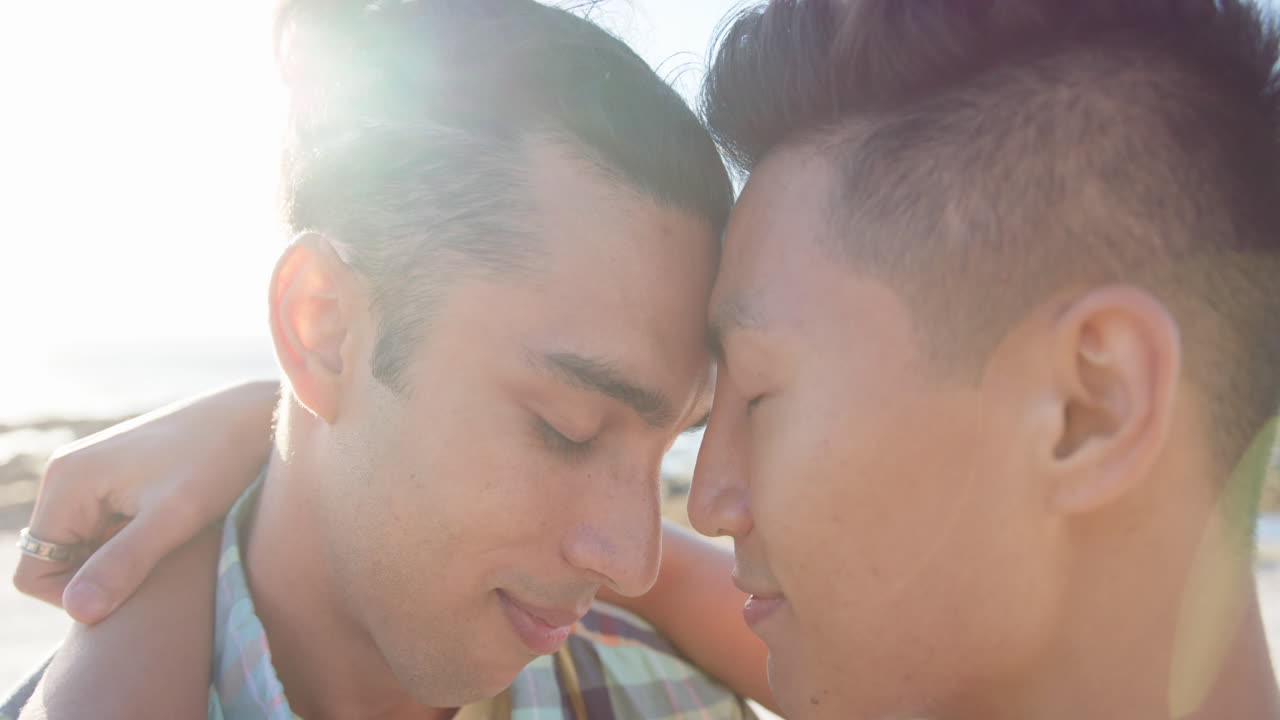 해변의 산책로에서 포옹하는 행복한 다양한 동성애 남성 커플, 슬로우 모션