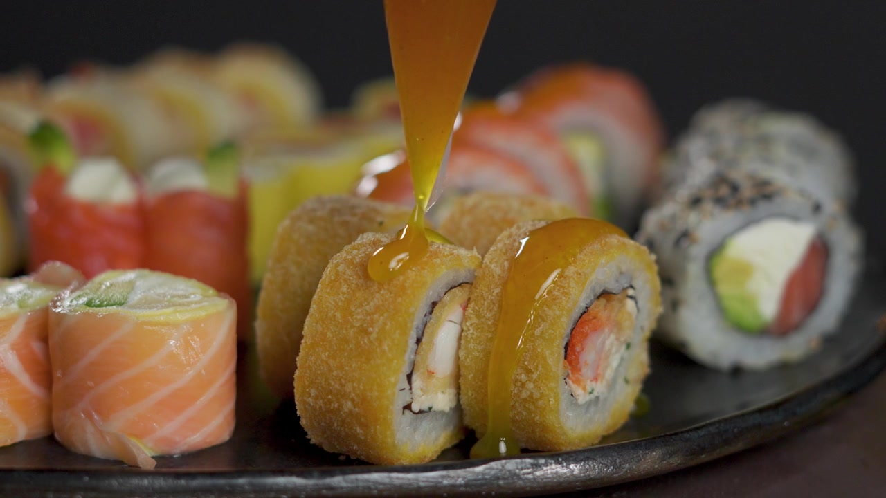 Lähikuva keltaisen mangokastikkeen kaatamisesta rapean tempura-sushirullan päälle.