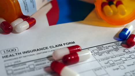 cancer drug pills falling on a prop medical insurance form showing high cost of chemotherapy treatment