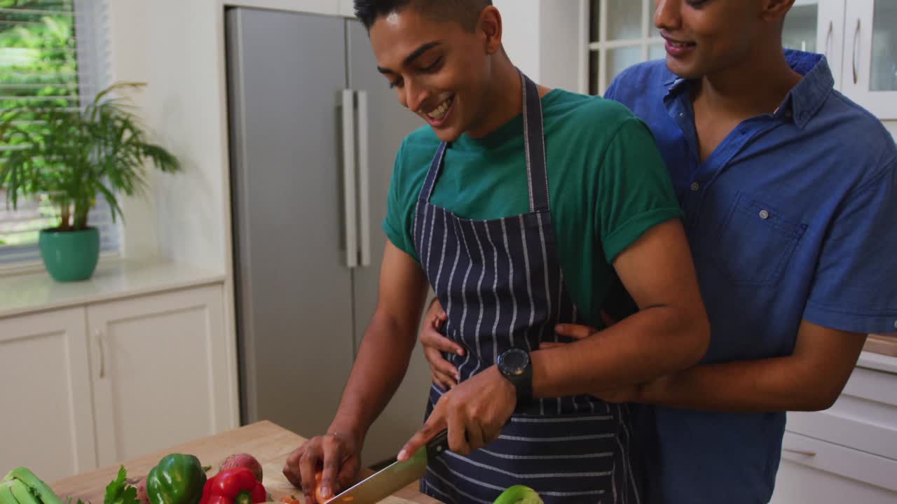 pareja de hombres gay de raza mixta feliz abrazándose mientras preparan comida en la cocina