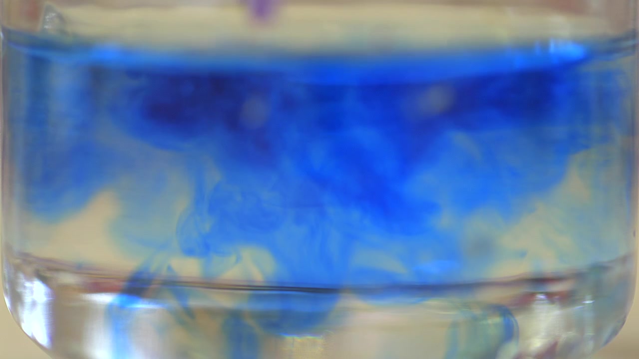 Close-up of blue ink dispersing in clear water, forming fluid abstract shapes and organic motion. Ideal for artistic backgrounds, creativity, science and visual effects.