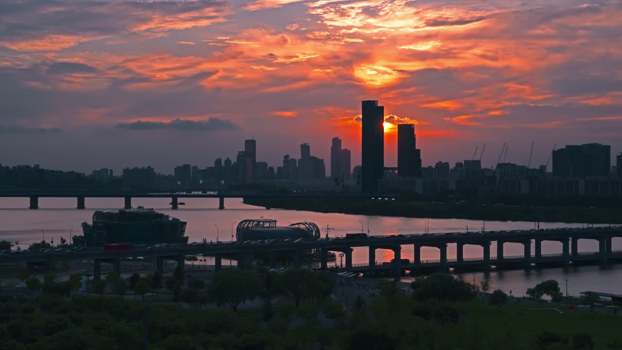 Aerial view of the sun setting directly behind a skyscraper in the Seoul skyline with traffic on Banpo Bridge and the Han River below