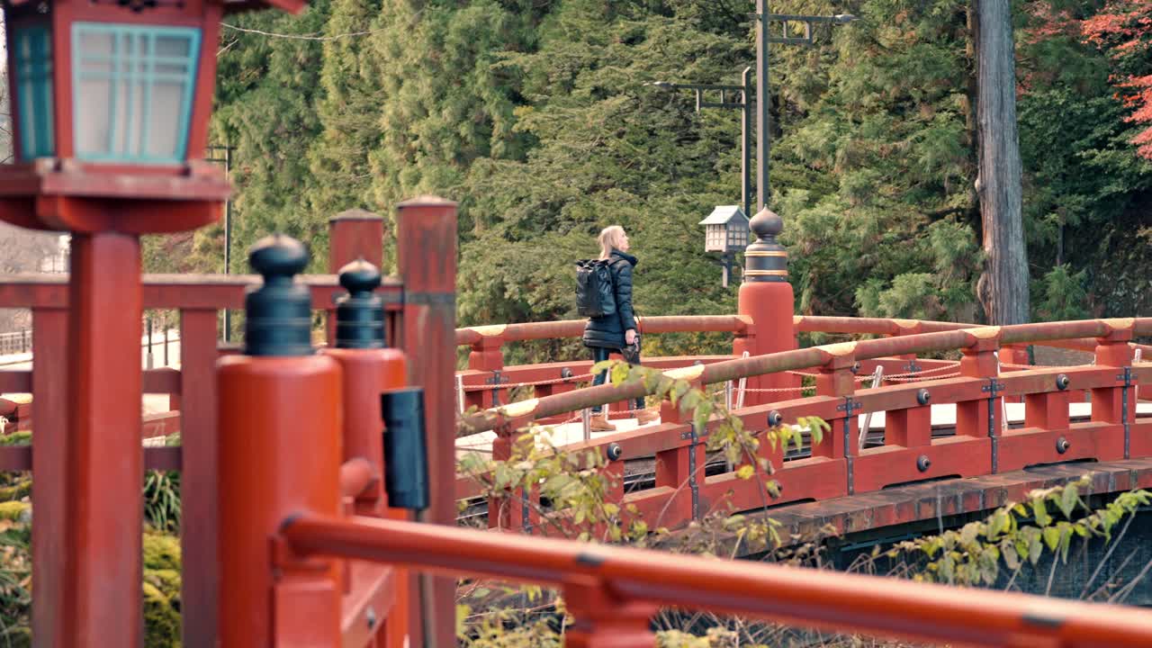 un momento sereno de una mujer rubia paseando por el icónico puente shinkyo en nikko, japón, rodeada de los cálidos tonos del follaje de otoño.