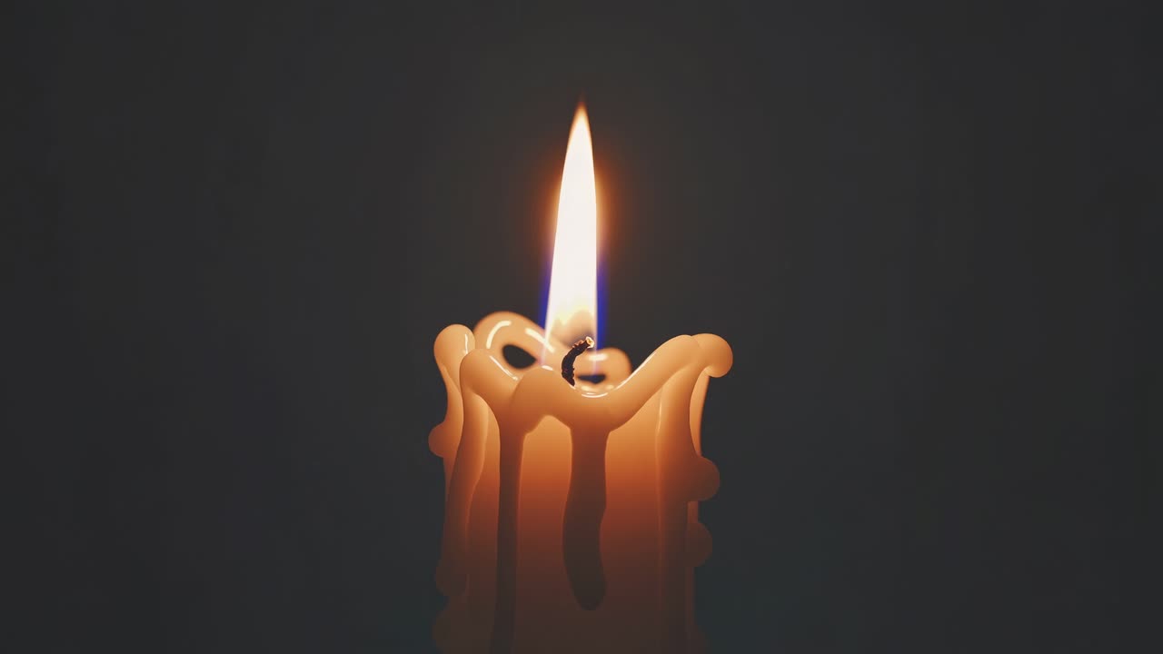 Close-up, low-angle shot of a lit candle with melting wax against a dark background