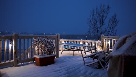 Eine-Hinterhofterrasse-In-Einer-Verschneiten-Nacht-Mit-Dem-Hellen-Sohn-Der-Veranda-Und-Dem-Schneebedeckten-Esstisch---Statische-Weitwinkelansicht