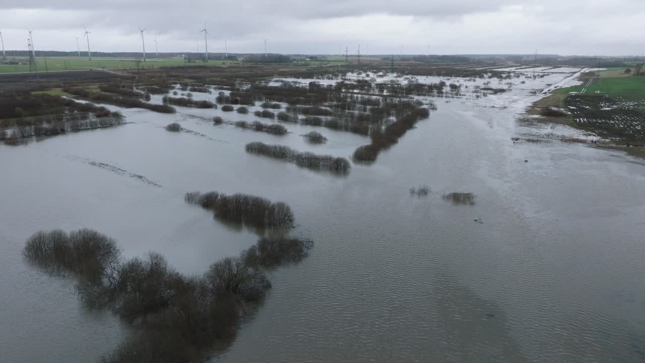 Aerial establishing view of high water in springtime, Alande river flood, brown and muddy water, agricultural fields under the water, overcast day, wide drone shot moving forward
