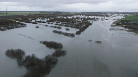 aerial establishing view of high water in springtime, alande river flood, brown and muddy water, agricultural fields under the water, overcast day, wide drone shot moving forward