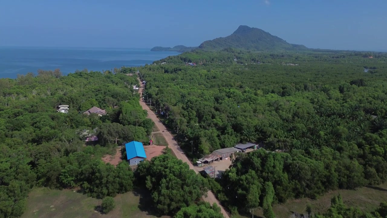 Volo di drone sopra la lussureggiante foresta tropicale dell'isola di Koh Jum nel sud della Thailandia. Una fitta vegetazione verde si estende su tutta l'isola con montagne visibili in lontananza, mostrando un'isola incontaminata