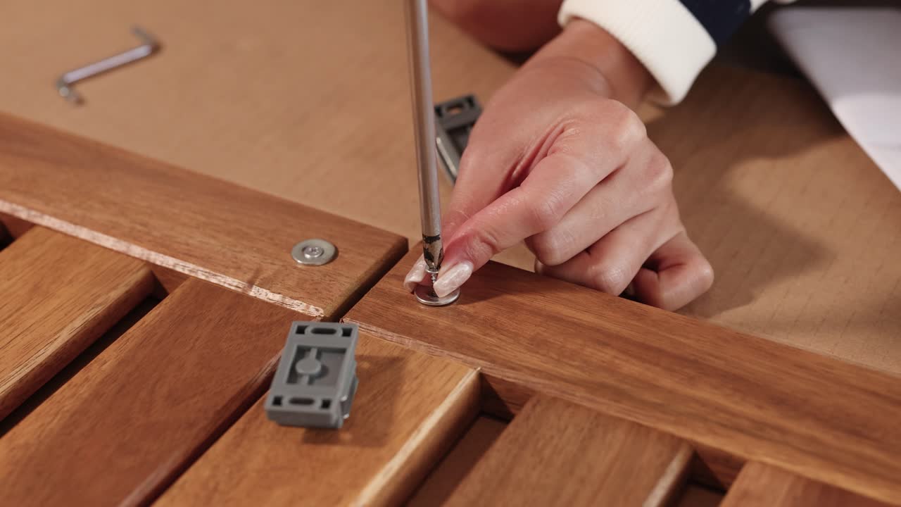 Close-up of hands assembling wooden furniture using a screwdriver and screws, highlighting precision and craftsmanship