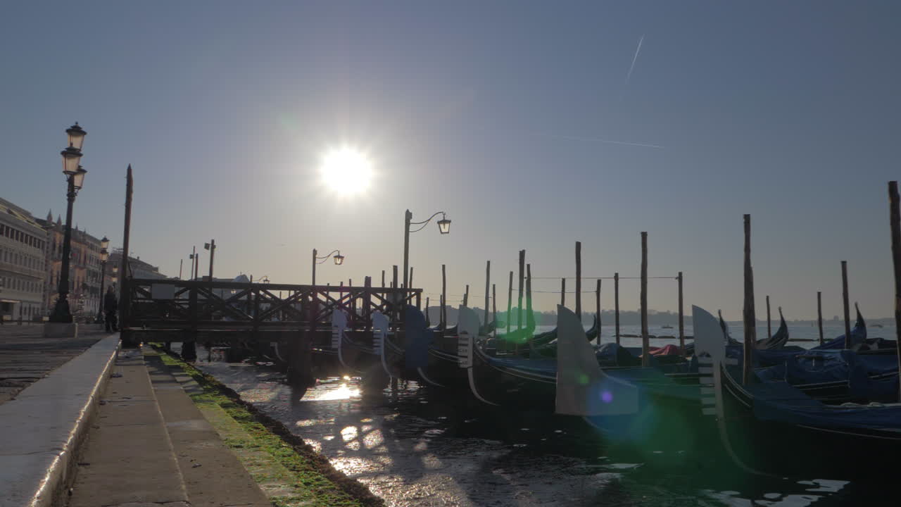 A slowmotion of gondolas swaying on a pier close to the paved Venice embankment