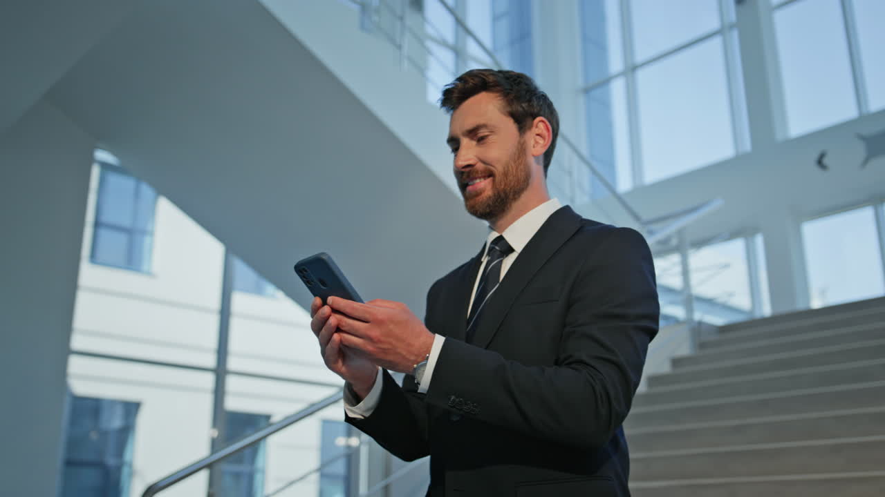 Smiling employee looking smartphone on staircase modern office building closeup