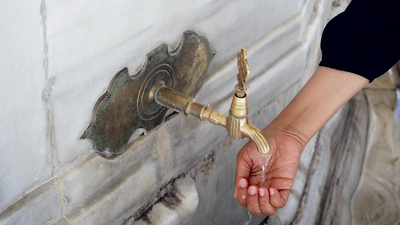 Persona che si lava le mani a una tradizionale fontana di marmo.