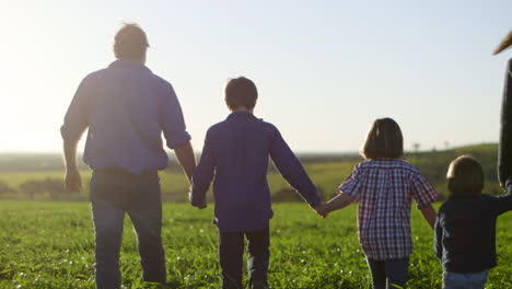 family walking away from camera in lush green field holding hands