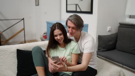 pareja sentados juntos abrazados en la cama usando un teléfono inteligente, dispositivo de desplazamiento