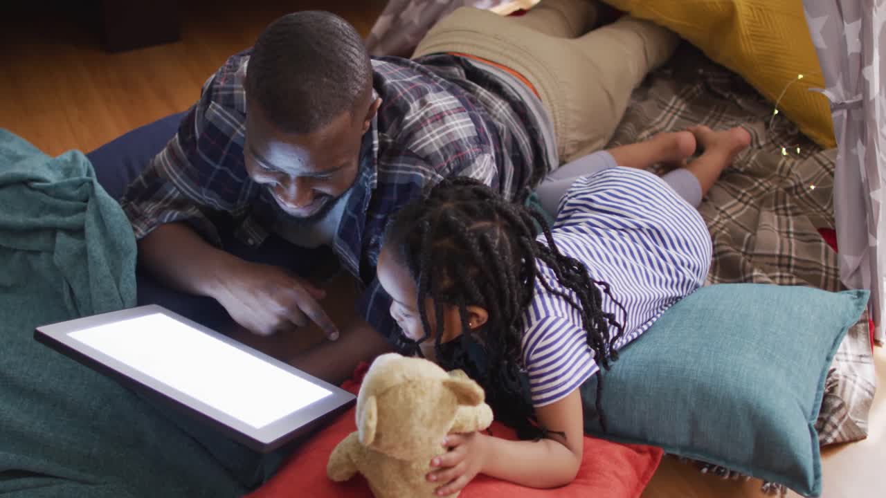 padre y hija afroamericanos felices acostados en la tienda y usando una tableta con espacio de copia