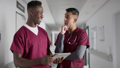 diverse male doctors discussing work, using tablet in corridor at hospital, slow motion