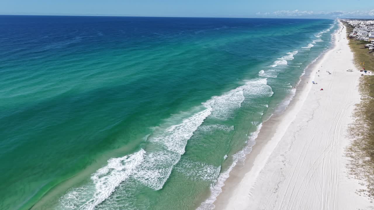Aerial orbit of turquoise Gulf of Mexico ocean waves rolling toward white sandy beach of 30A, Florida, USA