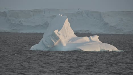 small ice berg in middle of ocean, with coastline in far background