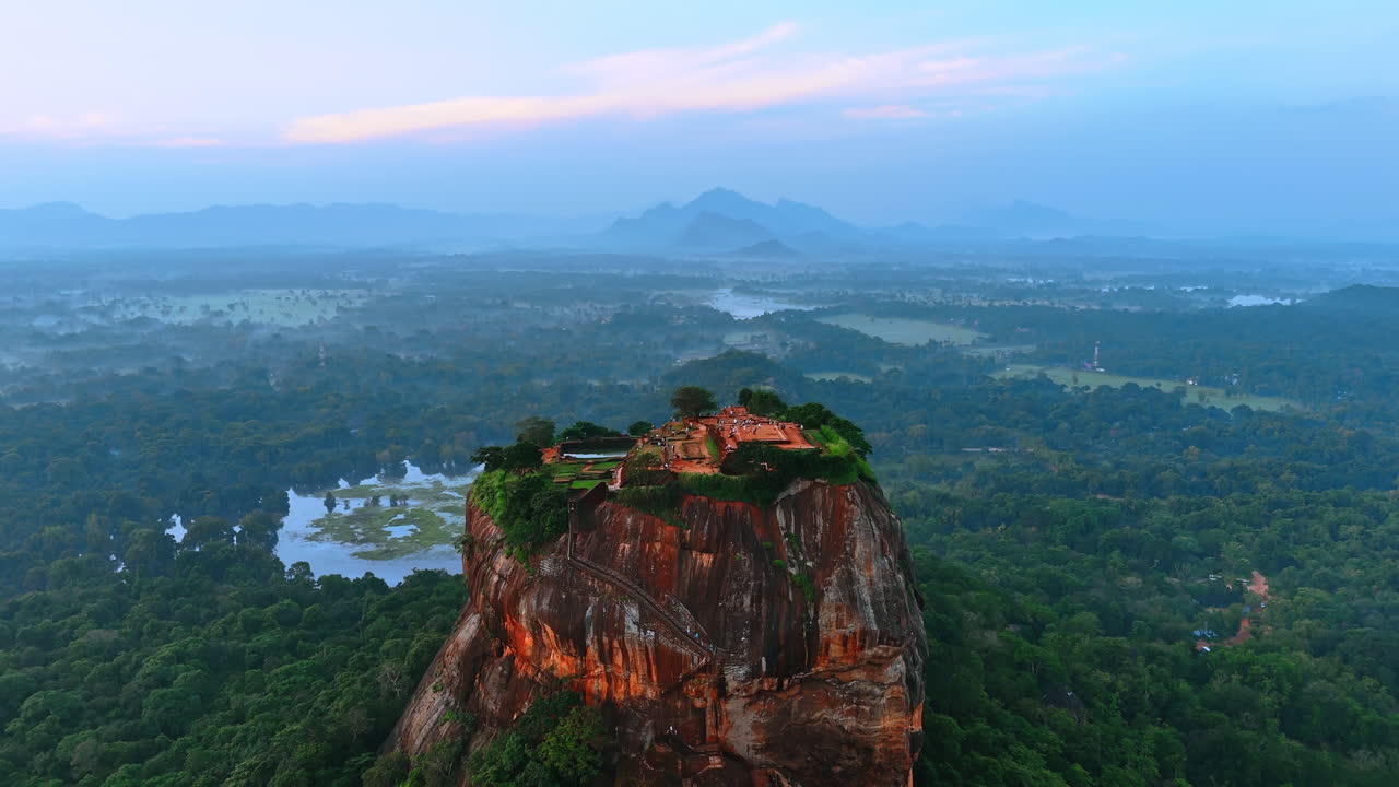 Numerous tourists walk by the ruins of fortress Sigiriya in Sri Lanka. Lion Rock from top view with hazy scenery at backdrop.