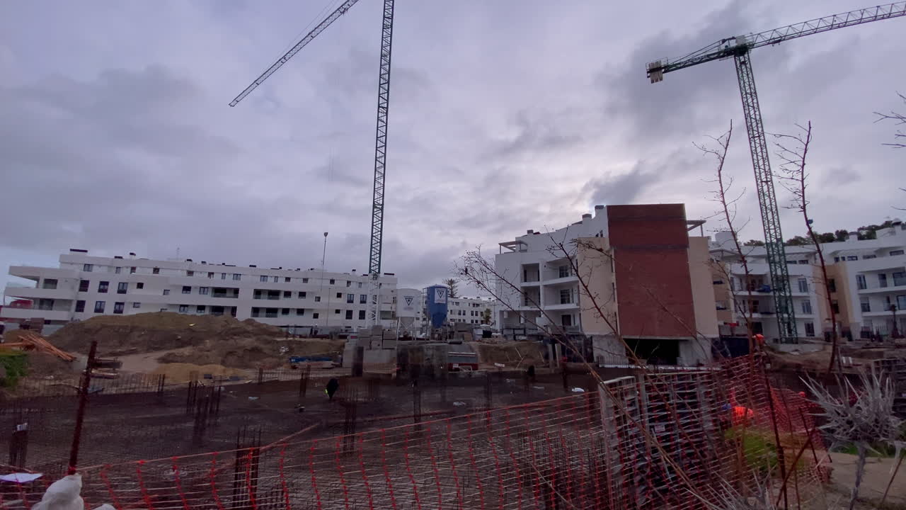 Obra en construcción con grúas torre desarrollando nuevos edificios de apartamentos e infraestructura residencial bajo un cielo nublado.