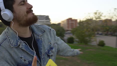 happy-man-dancing-with-earphones-on-and-mobile-phone-in-hand,-the-camera-turns-around-him