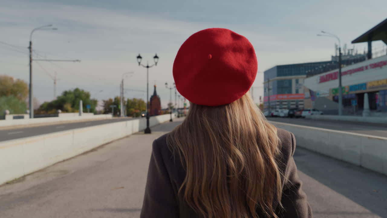 Calle tranquila de la ciudad durante una tarde de otoño. Mujer solitaria caminando por un puente urbano vacío al atardecer. Mujer de pelo largo con boina roja cruzando un puente de ciudad desierto durante el crepúsculo otoñal.