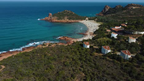 Flying-over-an-idyllic-natural-sand-beach-sandy-bay-on-the-tourist-vacation-island-Sardinia-in-Italy-with-sun,-clear-blue-turquoise-and-calm-water-close-to-La-Maddalena