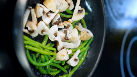 frying pan with beans and mushrooms in the oil. cooking veggies in the restaurant. close up. vertical screen.