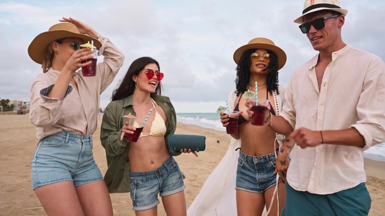Giovani amici felici che ballano e bevono cocktail sulla spiaggia