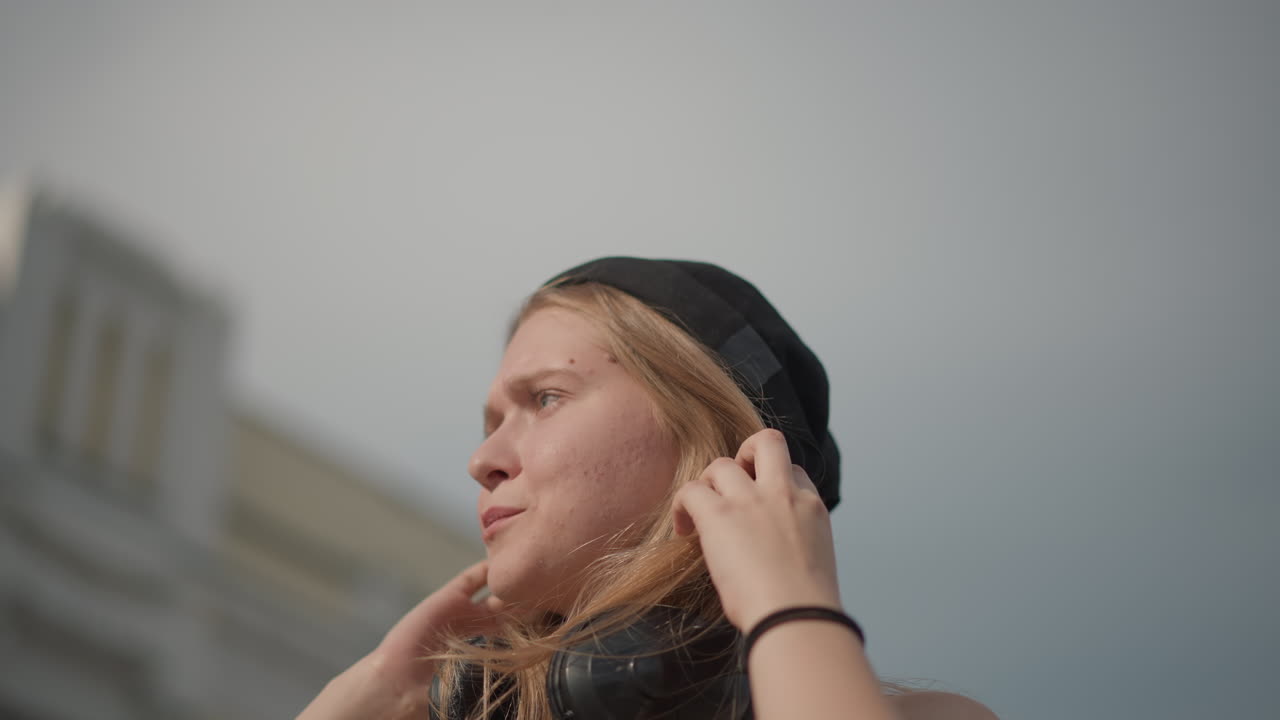 donna caucasica sorridente per strada che balla con le cuffie, filmato urbano energico che mostra movimenti espressivi e cenni giocosi con la testa, coreografia veloce e sguardo sicuro verso lo skyline, modifica