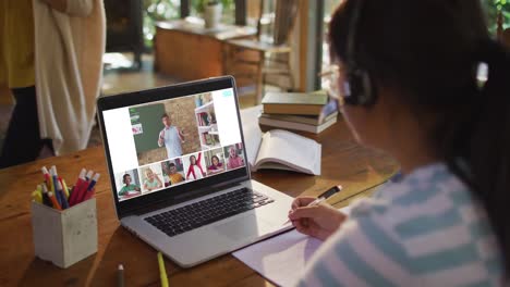 Schoolgirl-using-laptop-for-online-lesson-at-home,-with-diverse-teacher-and-class-on-screen