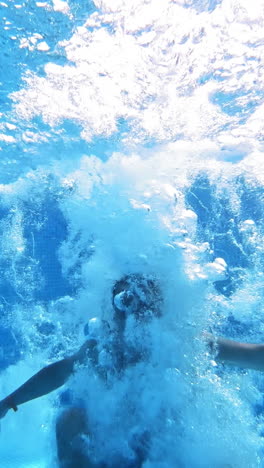 an energetic dive into a swimming pool. handsome young man swimming in pool, underwater view vertical video