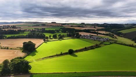 drone camera smoothly pans across vibrant green and golden fields near kinross, scotland, under dramatic cloudy skies with soft, natural daylight