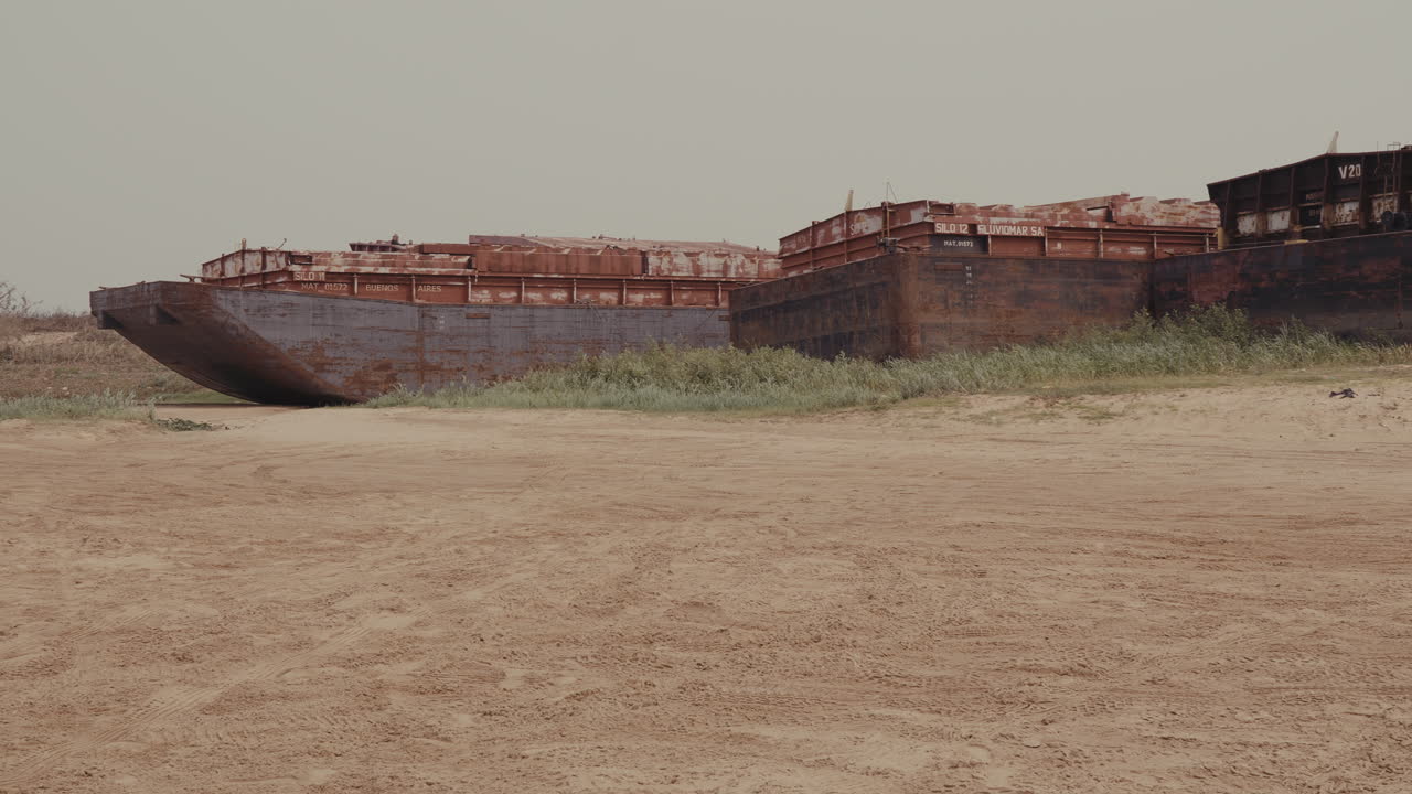 Abandoned Rusting Barges on Shoreline: Forgotten Industrial Giants in a Desolate Setting. Sandy foreground and overcast sky