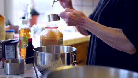 an elderly woman measuring ingredients and pouring them into a metal mixing bowl while baking a vegan chocolate cake dessert recipe