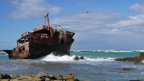 old weathered shipreck in shallows with waves running in, rocky coastline of l'agulhas, south africa, close-up static shot