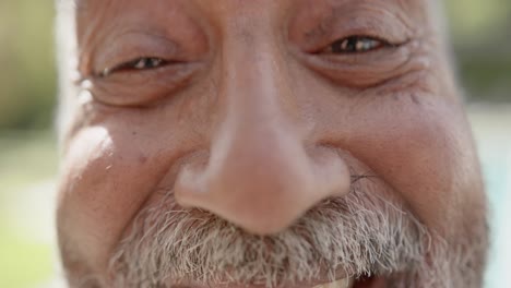 retrato de un hombre biracial mayor feliz mirando a la cámara y sonriendo en el jardín, cámara lenta